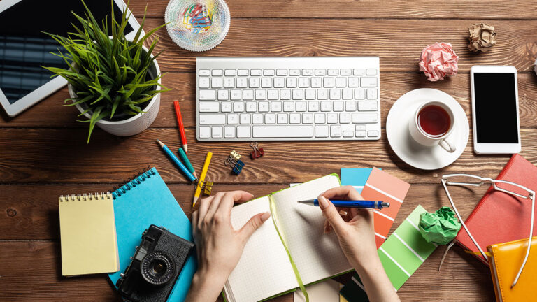 A desk filled with swatches, papers, notebook, and coffee.